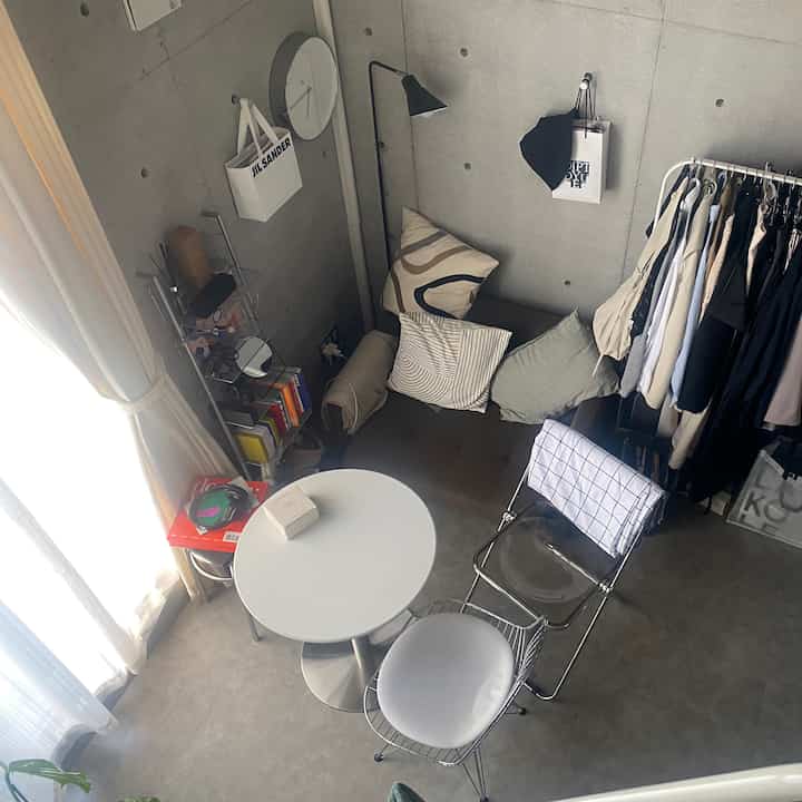 白とグレーのトーンのワンルーム、コーナーソファベッドとラウンドカフェテーブル、椅子が配置されたモダンでコンパクトな空間