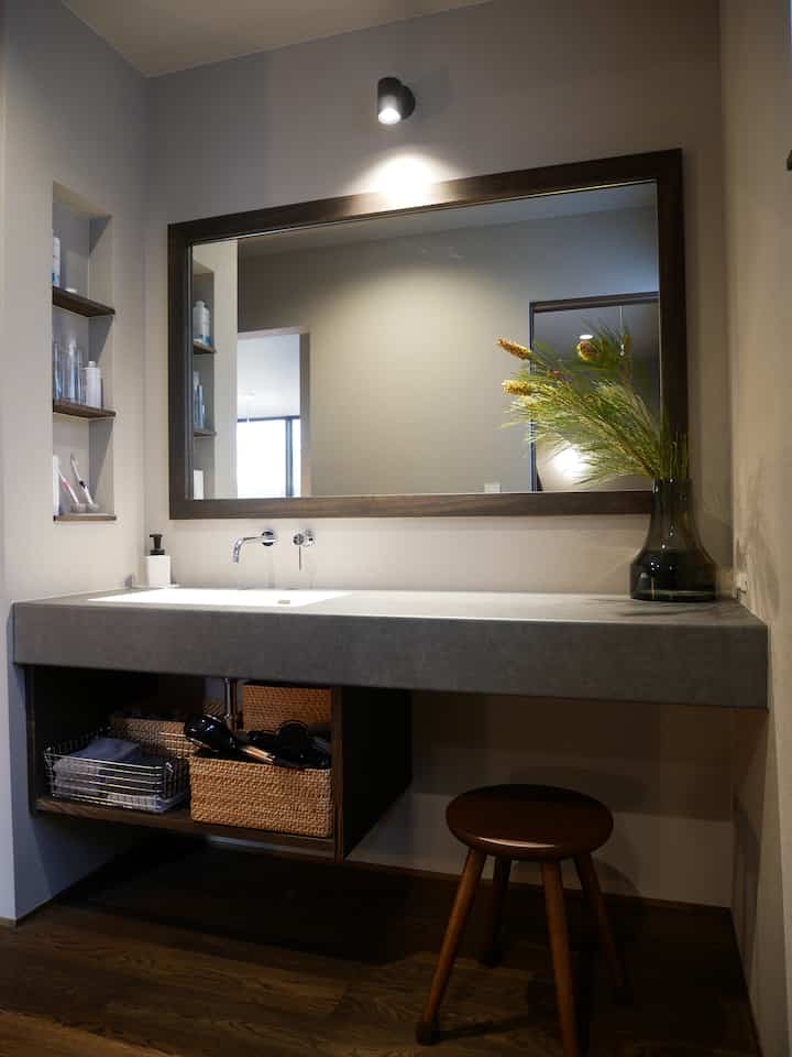 Natural-toned bathroom space featuring a large mirror, washbasin, and wooden stool with cozy atmosphere