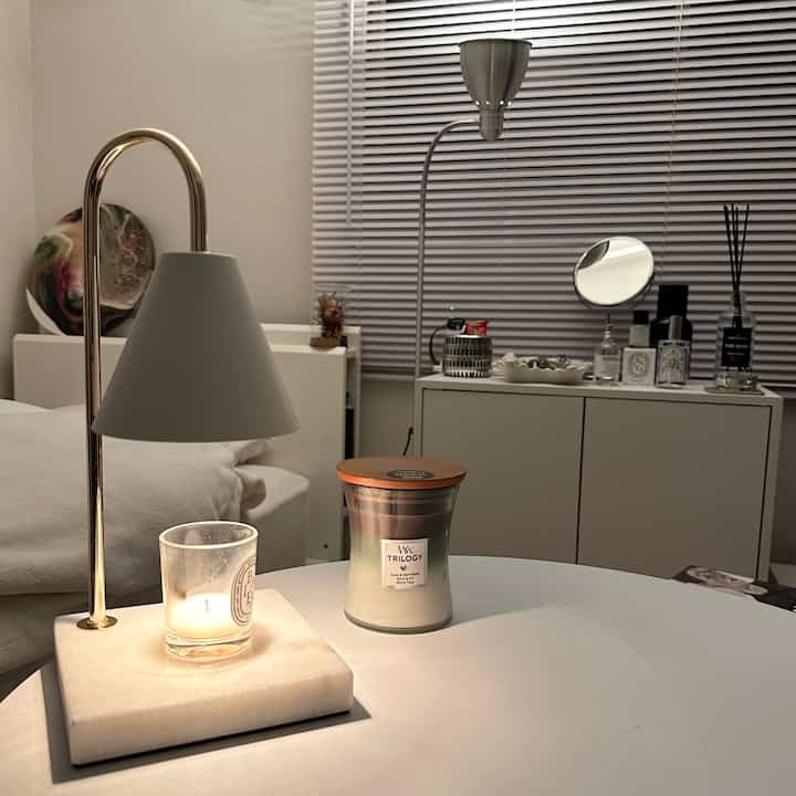 白を基調としたリビングまたはリラックス空間、キャンドルとディフューザーが置かれたサイドテーブルとフロアランプが調和したインテリア