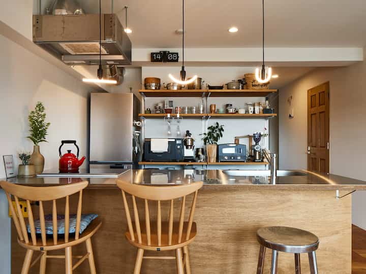 ナチュラルな色調のコンパクトなキッチン空間、木製のダイニングチェアとステンレスカウンター、赤いケトルが印象的な清潔感のあるインテリア