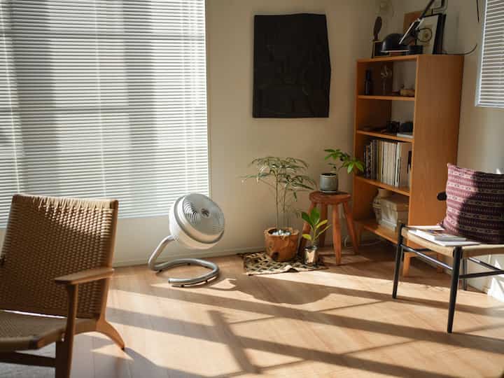 明るい白いブラインドとブラウンの木調家具が配置された自然光あふれるミニマルなリビング空間