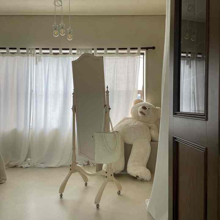 Bright white-toned living room featuring a standing mirror and a large beige teddy bear in a minimalist style interior
