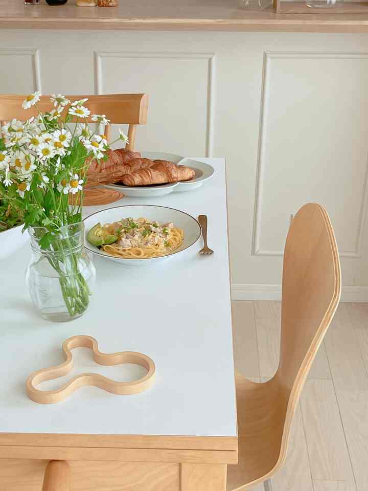 ナチュラルトーンのダイニングルーム、木製の椅子と白いテーブルに花瓶と食事が配置された雰囲気のある空間