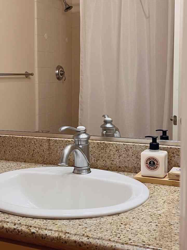 White and beige toned bathroom sink with silver faucet and shower curtain, creating a clean bathroom atmosphere