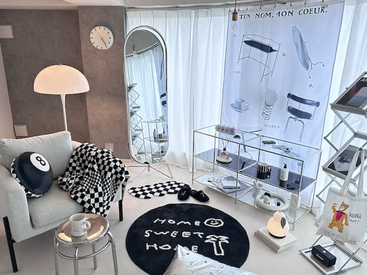 白と黒のトーンのモダンなリビング、洗練されたスツールと大型の鏡、チェッカーパターンのアクセサリーが配置された空間