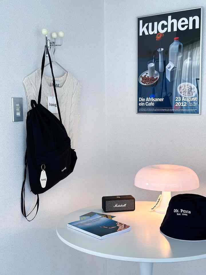A space with white walls and a round table, featuring an Artemide Nesso lamp, a black backpack, and a hat on the table in a neat interior