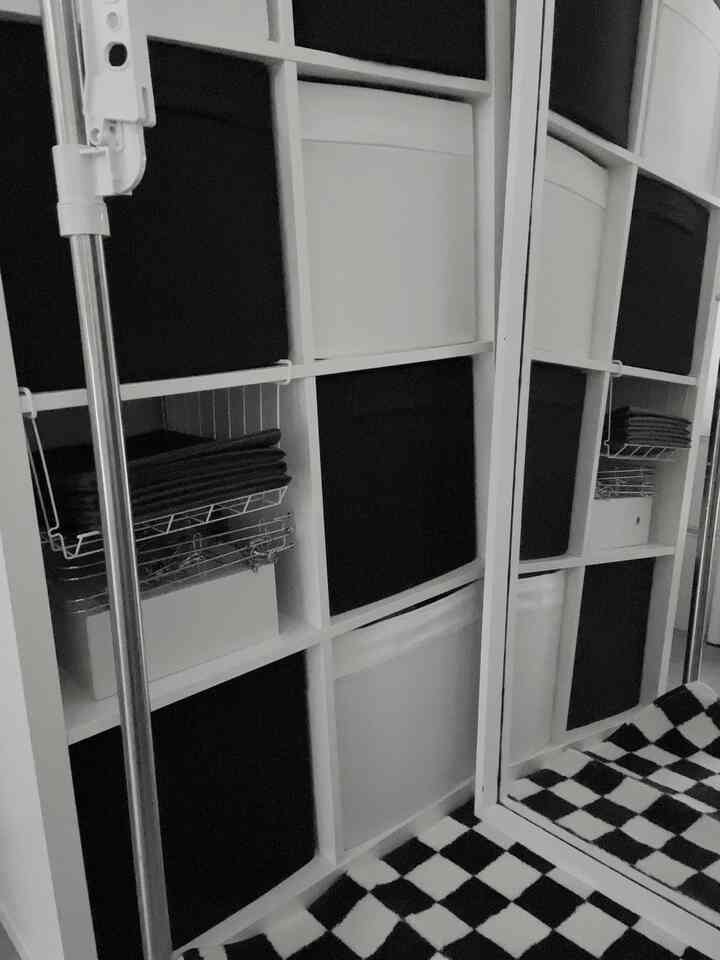 白と黒のモノトーンの狭い部屋、チェッカーボードマットと収納ボックスが配置された清潔感のある空間