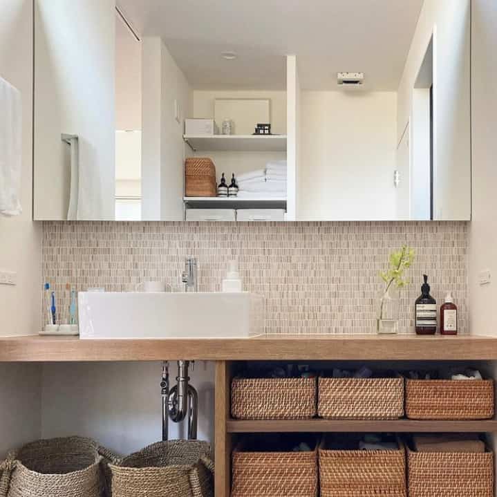 Bathroom with beige tiled wall and wooden countertop, featuring rattan baskets and towels neatly arranged in a natural style