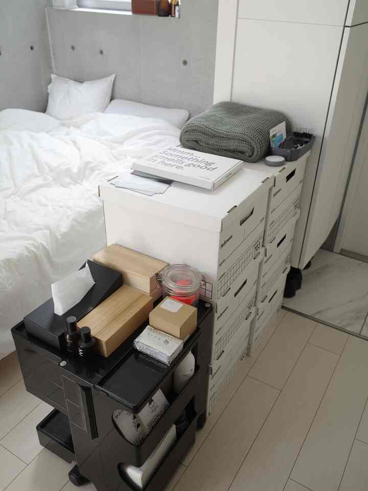 White-toned compact bedroom featuring a bed and stacked white storage boxes on the floor, creating a tidy and organized atmosphere