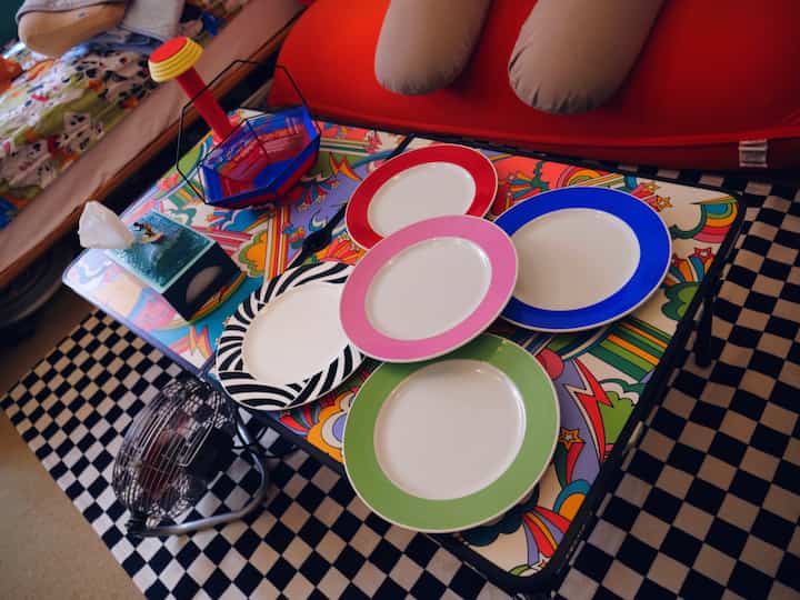 カラフルな皿が並ぶ柄入りテーブルと鮮やかな赤いソファが配置された雰囲気のある空間