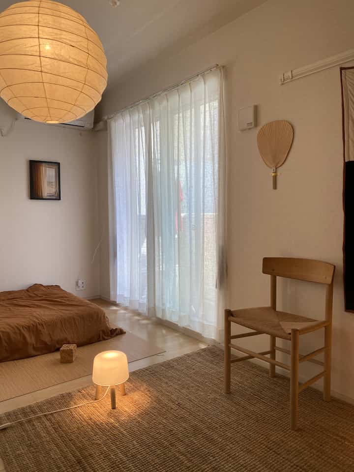 暖かいベージュトーンと木製家具が配置された居心地の良い一人暮らしのリビングと寝室の空間