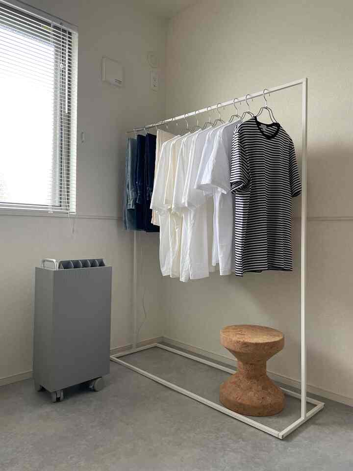 シンプルな白を基調とした狭い部屋、白いメタルのハンガーラックとコルク製のスツールが配置された清潔感のある空間