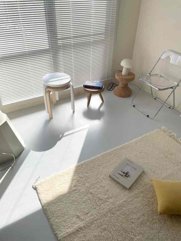 明るいホワイトとベージュ調のコンパクトなリビングルーム、透明な椅子とスツール、ラグ、温かみのある照明が配置された印象的な空間