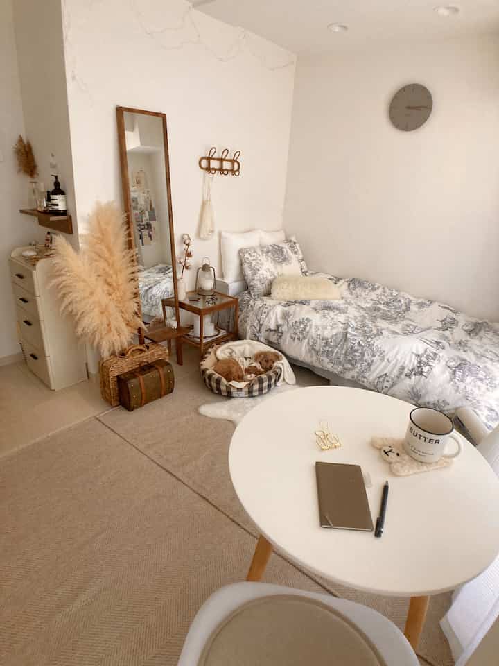 ナチュラルトーンの寝室、丸テーブルとベッド、犬のペットベッドが配置され、温かみのある整った空間