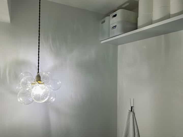 ホワイトトーンの壁と棚、バブルランプが美しく照らすシンプルで整頓されたトイレ空間