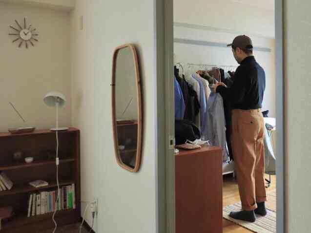 白い壁と木目調家具が調和する玄関、壁掛けミラーと時計、シンプルに配置されたハンガーラックが特徴的な空間