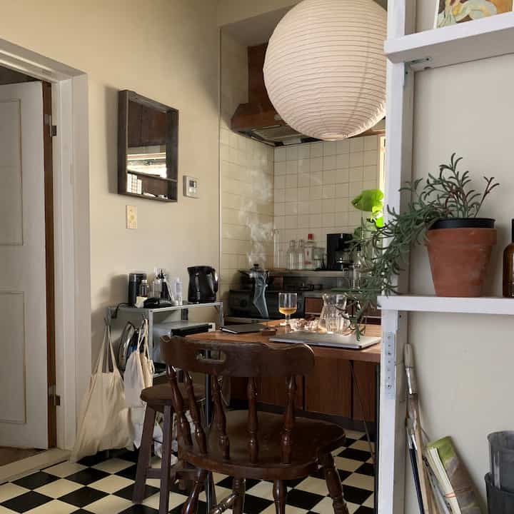 ライトブラウンとグレー調のヴィンテージキッチン、木製のダイニングテーブルと椅子、植物、紙製のランプシェードが配置された雰囲気のあるインテリア