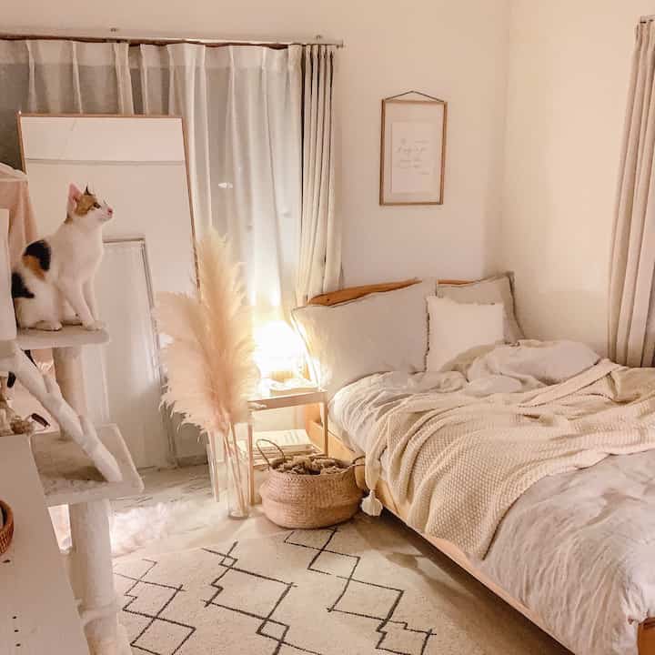Natural toned bedroom featuring wooden bed, cat tower, and rug creating a cozy atmosphere