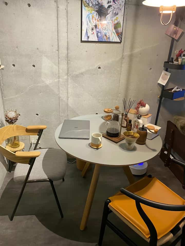 ライトグレーと木目調のモダンな小さなホームカフェ空間、グレーの丸テーブルと二つのアームチェアが配置された居心地の良いインテリア
