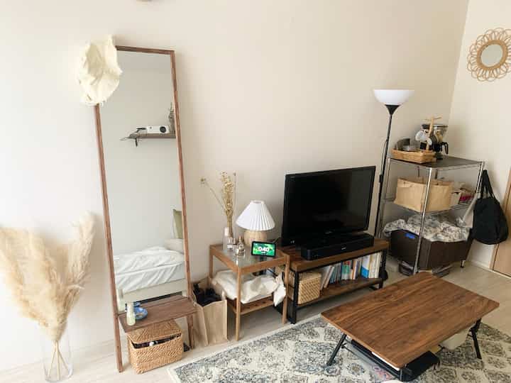 ベージュ色の壁と木目調の家具、姿見が配置されたナチュラルスタイルのワンルームのリビング