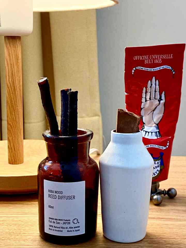 Natural tone bedroom with L-shaped window, wood tone side table featuring diffuser and hand cream in a cozy setting