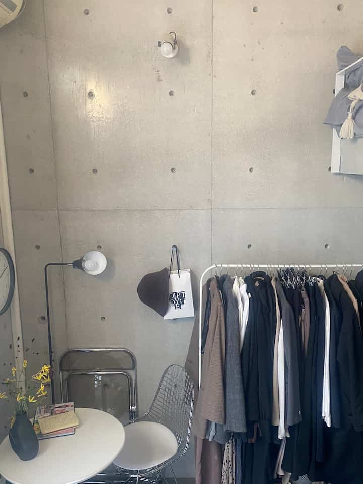 グレーのコンクリート壁と白い丸テーブル、服掛けが配置されたコンパクトなワンルームのインテリア