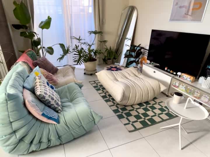 白と緑の色調のリビングルーム、ライトブルーのソファとプフ、植物、サイドテーブルが配置された雰囲気のあるインテリア