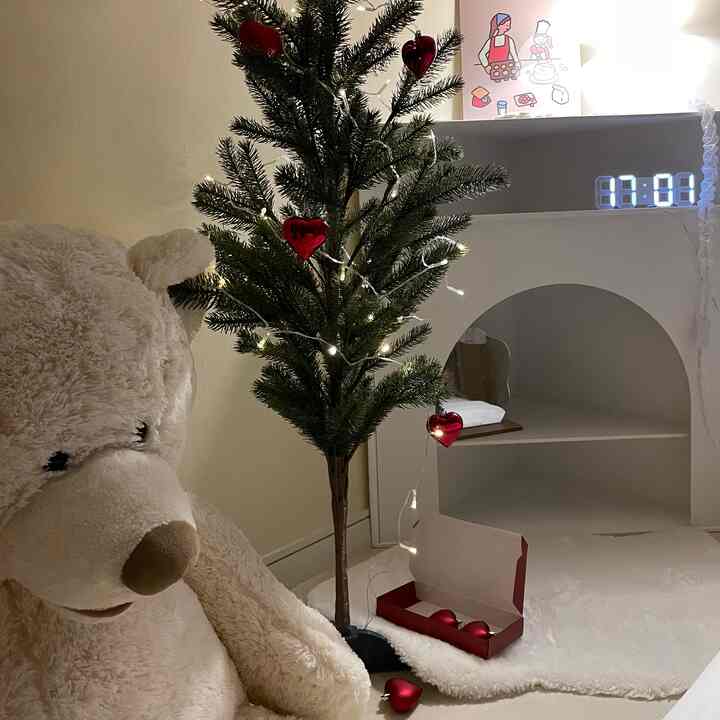 ナチュラルカラーとホワイトトーンのリビングルーム、クリスマスツリーと大きなぬいぐるみベア、かわいいポスターが配置された雰囲気のあるインテリア