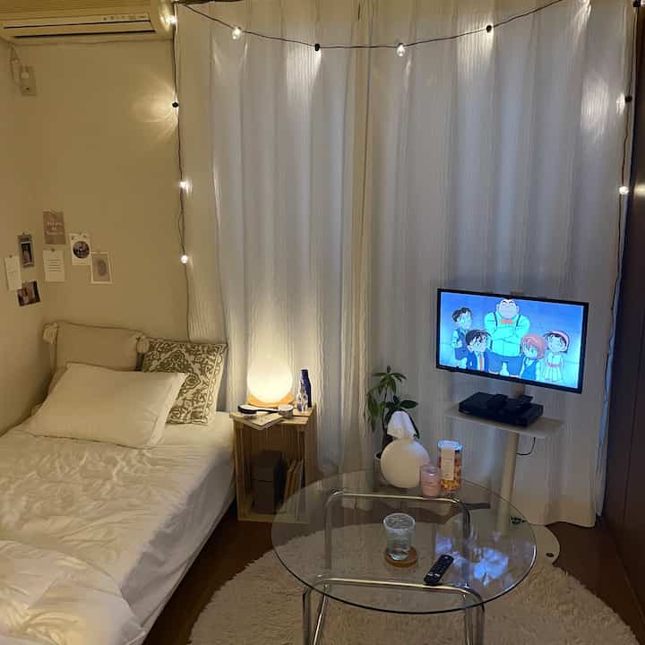 White and natural-toned single household living room and bedroom with string lights and ambient lamp creating a cozy atmosphere