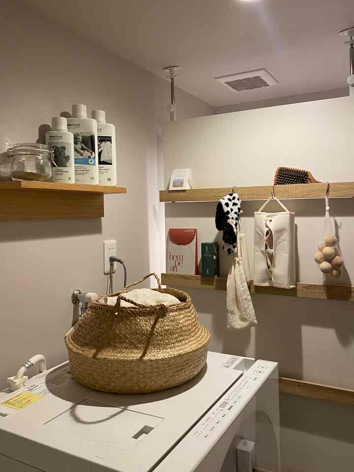 ナチュラルな色調の狭いバスルーム、中央に洗濯機が配置され、木目調の棚と収納アイテムが調和した雰囲気のあるインテリア