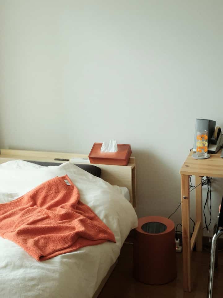 Natural-toned bedroom with orange accents, featuring a wooden desk, orange towel, and trash can creating a cozy atmosphere