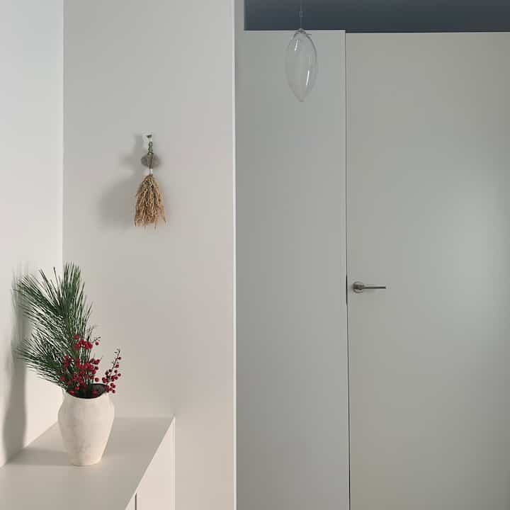 白とナチュラルな色調の玄関空間、左の棚に植物と花瓶が配置されたシンプルなインテリア