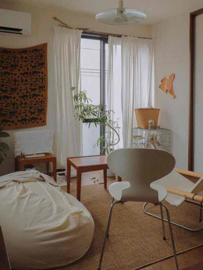 White and brown toned small living room featuring bean bag sofa, armchair, plant, and coffee table in a natural style