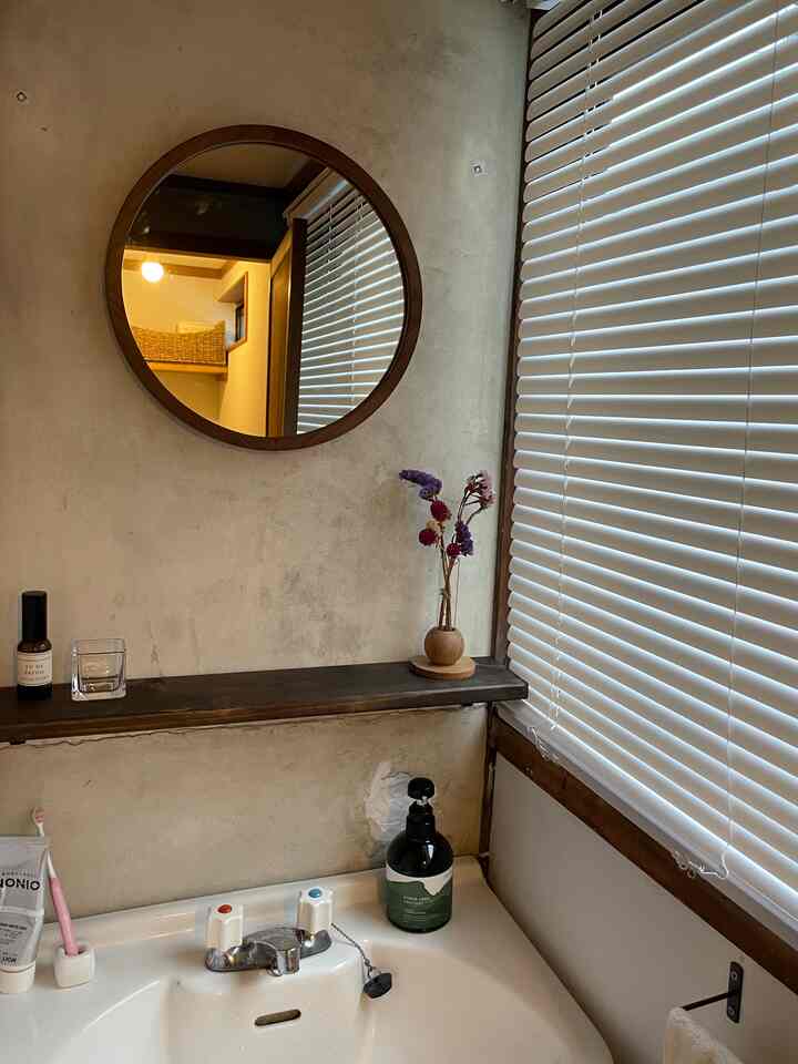 ナチュラルな色調のバスルーム洗面スペース、丸い木製フレームの鏡と木の棚が配置された雰囲気のあるインテリア