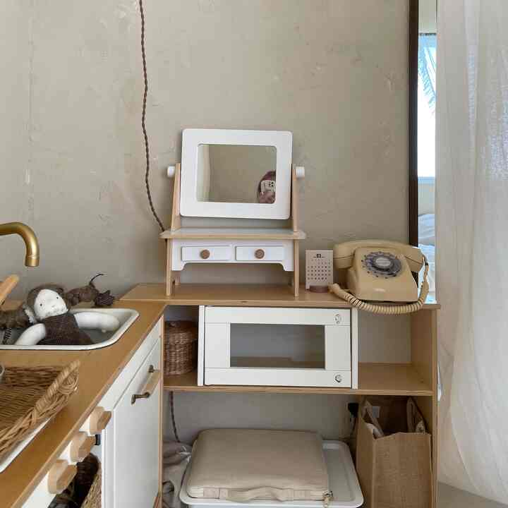ベージュと木目調の色合いの子供部屋、ミニキッチンセットと人形、レトロな電話が配置された雰囲気のあるインテリア