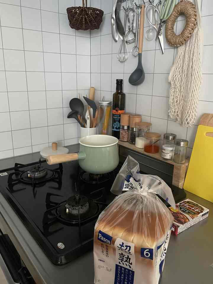 白いタイル壁と黒いガスコンロがあるキッチン、緑色の鍋と調理器具が配置された雰囲気のある空間