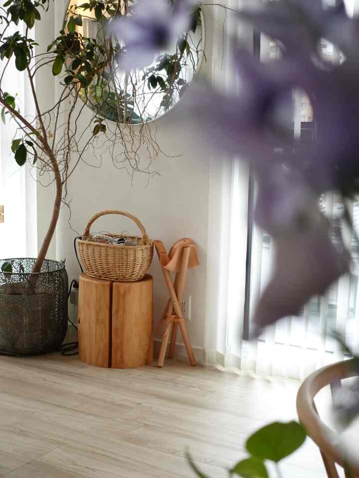 自然な木目調と白い背景のコーナースペース、木製スツールの上にかごと観葉植物が置かれた清潔感のあるインテリア