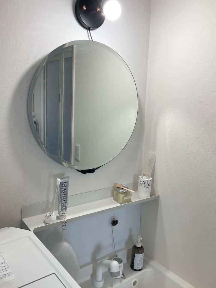 白を基調としたバスルーム、丸い鏡と棚に整理された洗面用品が配置されたミニマルで清潔感のあるインテリア