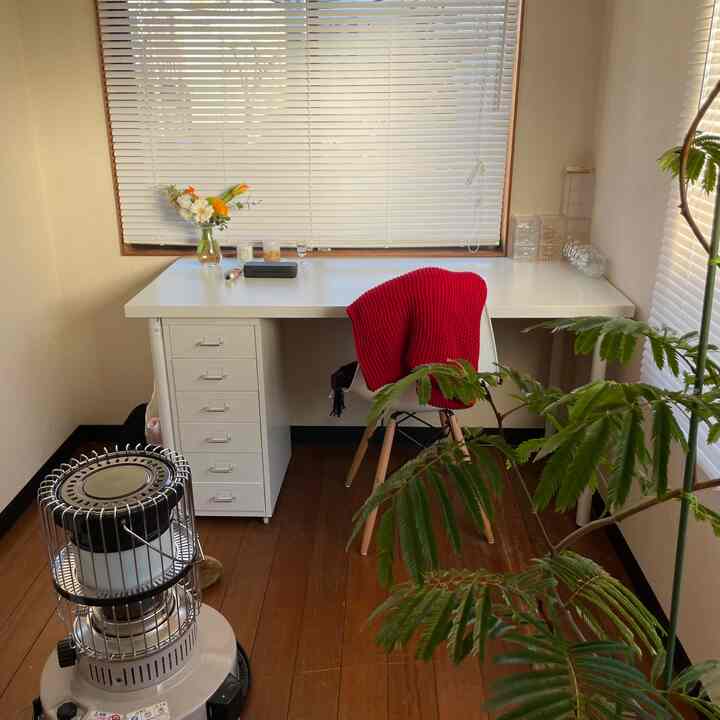 白いデスクと茶色の床、赤いブランケットがかかったオフィスチェア、緑の植物が配置された落ち着いたホームオフィスのインテリア