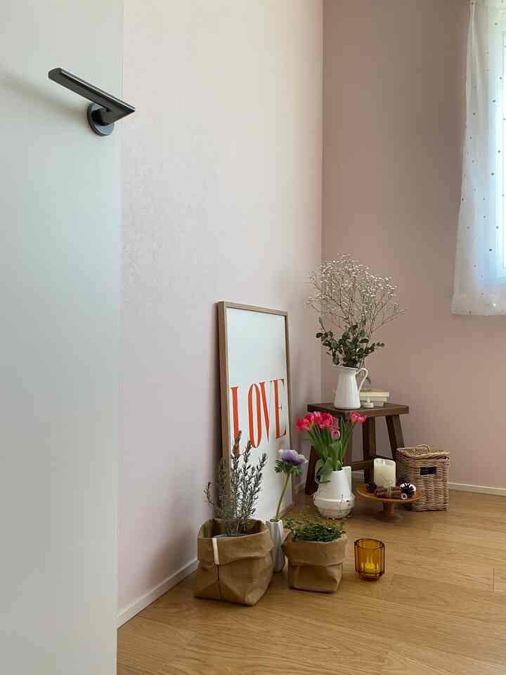 Pastel pink wall and beige wood floor form a kids' room photo booth corner featuring vases and natural decor elements