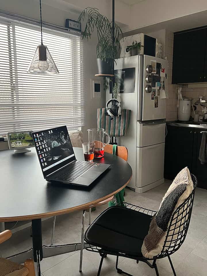 Black and gray toned compact dining room featuring a round dining table, pendant light, and a laptop for remote work setup