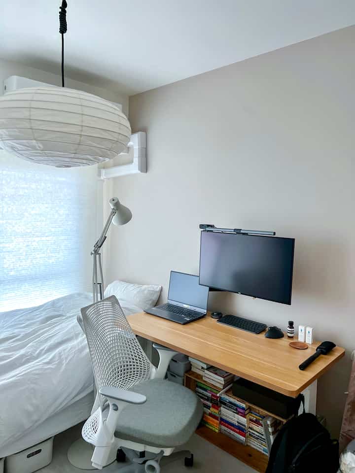 Bright natural-toned studio workspace with white bed and light brown desk, modern and minimalistic design