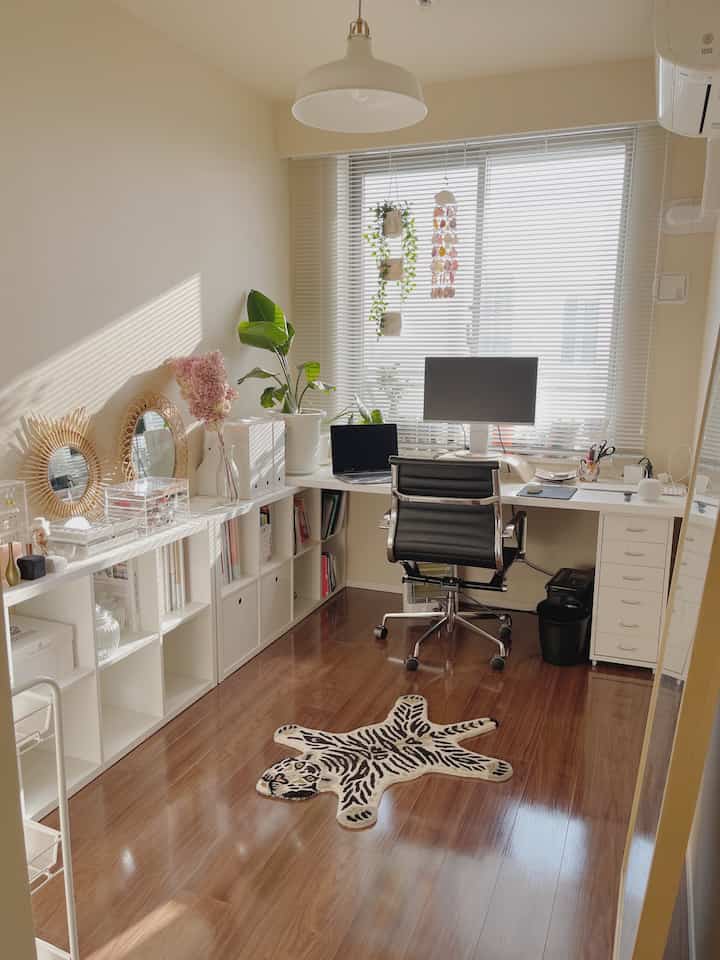 明るい白と茶色のトーンの小さなホームオフィス、デスクとエルゴノミクスチェア、ラタンミラー、タイガーパターンのラグ、植物が配置された印象的な空間