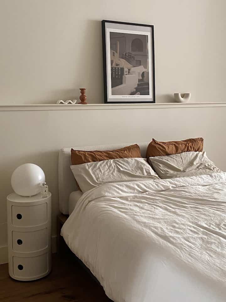 Beige and white toned bedroom featuring a white bed with brown pillows, a nightstand, and modern art poster creating a calm ambiance
