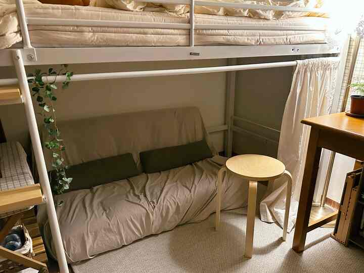 Natural small bedroom with white and wood tones, featuring a sofa bed and minimal wooden stool