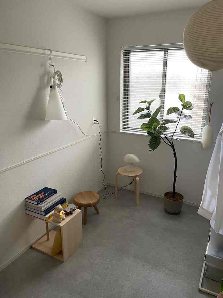 Natural-toned small room featuring a plant by the window, wooden stool, and floor lamp in a simple setting