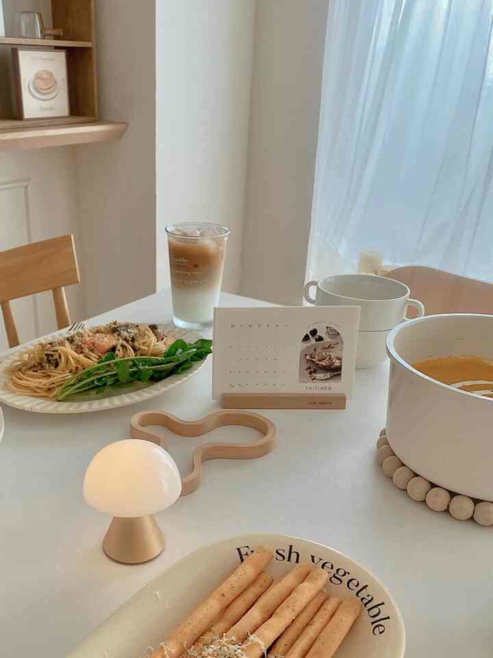 柔らかなベージュと白の色調のキッチン、透けるカーテンと木製の椅子が配置されたシンプルで自然なインテリア