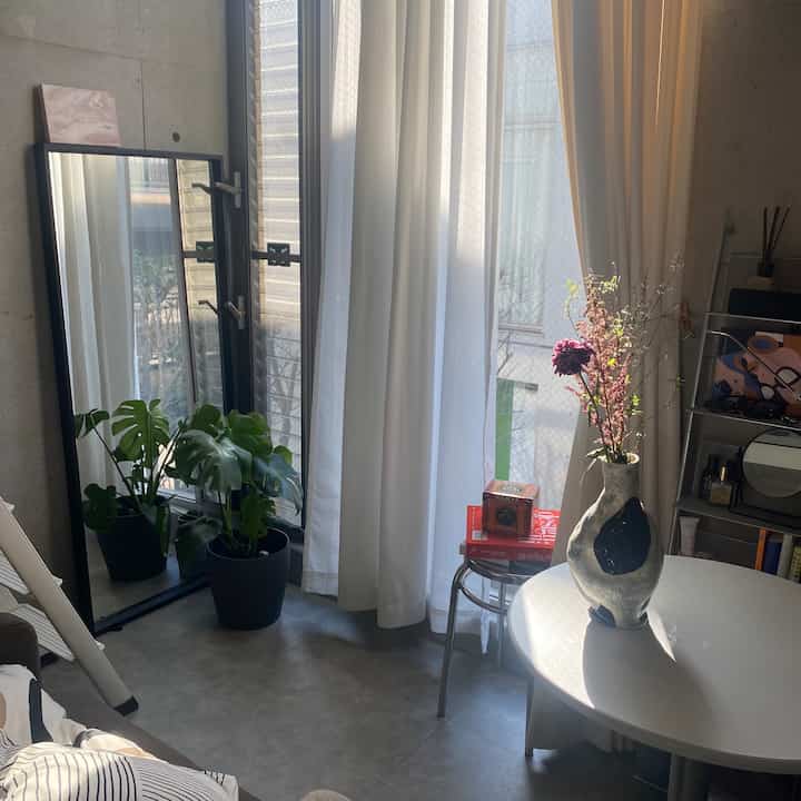 White and natural toned living room featuring curtains, indoor plant, and a modern vase on a round table