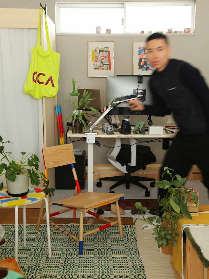 Bright white walls and wood-tone furniture in a compact home office space, featuring a stool and vibrant plants