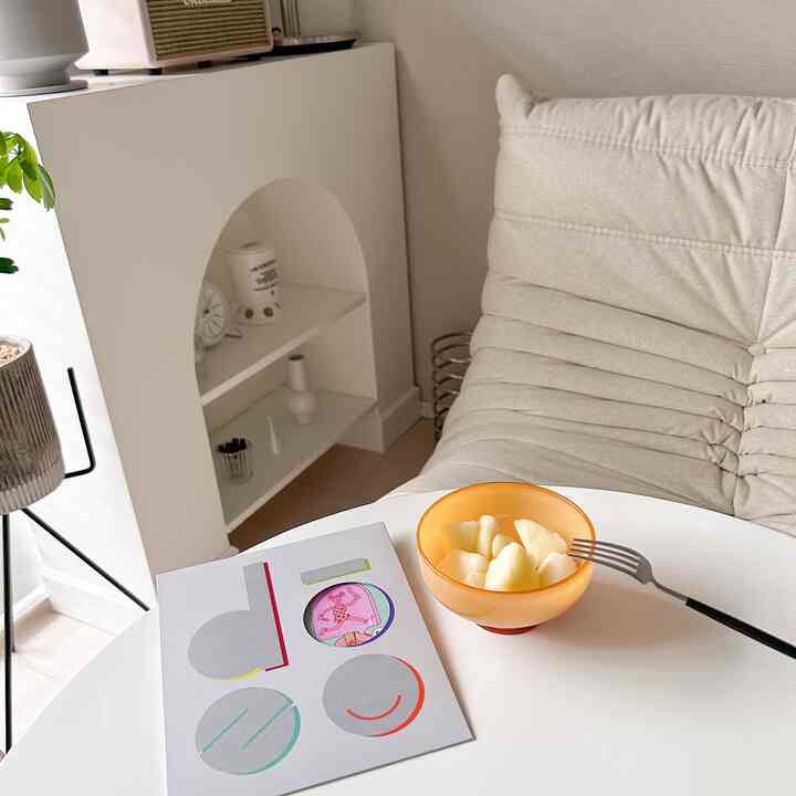 Natural-tone small studio apartment featuring a beige sofa and white table with plate and fruit, creating a cozy home cafe atmosphere